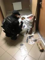 funkcjonariusz celno-skarbowy przy workach z papierosami i suszem; obok na podłodze kastet i pistolet