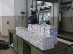 3,4 tys. paczek papierosów leżących na ladzie w budynku kontroli szczegółowej; w głębi funkcjonariusz Służby Celno-Skarbowej