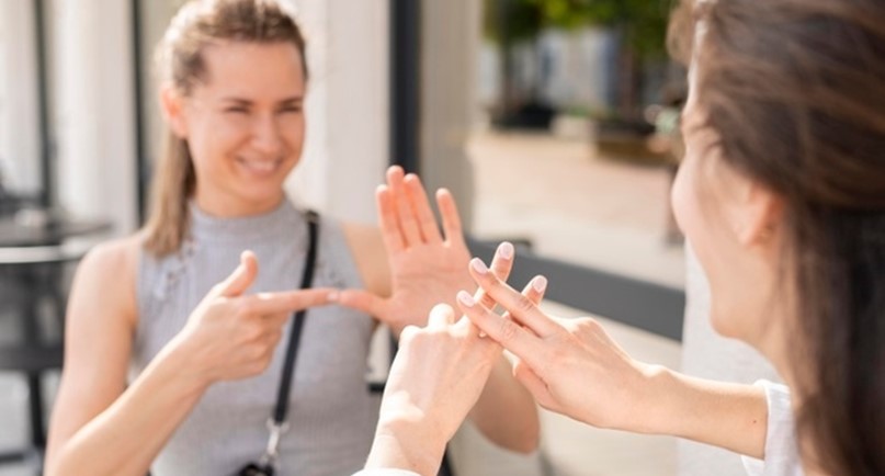 Dwie uśmiechnięte kobiety rozmawiające w języku migowym