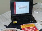 Na zdjęciu otwarty laptop z wyświetlaną na ekranie prezentacją, obok na stole leży żółta książka o podatkach.