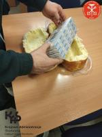 funkcjonariusz - widoczne ręce - wyjmuje papierosy z rozkrojonej bułki