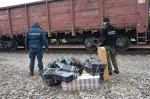 na pierwszym planie stoją funkcjonariusz Służby Celno-Skarbowej i Straży Granicznej przy ułożonych na ziemi pakunkach z papierosami; w tle widoczny wagon towarowy