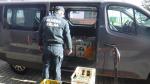 Funkcjonariusz Służby Celno-Skarbowej stoi przy busie. Obok niego i wewnątrz busa ustawione skrzynki z butelkami z alkoholem