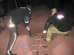 Funkcjonariusze Służby Celno-Skarbowej i Straży Granicznej podczas wyjmowania papierosów z ładunku rudy żelaza. Funkcjonariusze stoją w wagonie. Jest pora nocna.