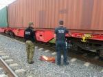 funkcjonariusz Straży Granicznej i Służby Celno-Skarbowej stoją przy pociągu towarowym; na ziemi leży worek ze znalezionymi papierosami