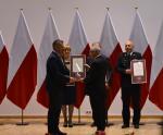 Dyrektor Izby Administracji Skarbowej w Lublinie odbiera dyplom uznania z medalem od Wojewody Lubelskiego. W tle flagi Polski.