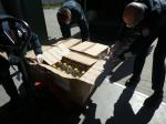 Trzech funkcjonariuszy służby celno-skarbowej rozpakowuje kartony zawierające butelki z alkoholem