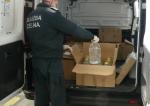 Funkcjonariusz Służby Celno-Skarbowej pakujący do samochodu kartony z butelkami wypełnionymi bezbarwna cieczą.