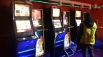 Trzy ustawione obok siebie automaty do gier hazardowych. Włączone, na wyświetlaczach widać kolorowe napisy i obrazki. przed automatami stoi funkcjonariusz SCS.