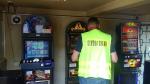Funkcjonariusz Służby Celno-Skarbowej stojący tyłem. Przed nim soja trzy automaty do gier hazardowych.