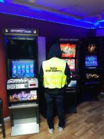 Funkcjonariusz Służby Celno-Skarbowej stoi przy trzech automatach hazardowych.