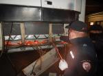 funkcjonariusz Służby celno-Skarbowej stoi przy naczepie ciężarówki i wyciąga z przerobionej podłogi papierosy; papierosy umocowane są na specjalnych szelkach