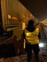 Noc, tory kolejowe. Przy jednym z kontenerów stoi funkcjonariusz Służby Celno-Skarbowej. Obok niego leży kilkanaście kartonowych pudeł. 