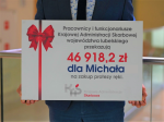 Tablica z napisem: pracownicy i funkcjonariusze krajowej administracji skarbowej województwa lubelskiego przekazują 46 918,2 zł dla Michała na zakup protezy ręki.