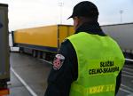 Funkcjonariusz Służby Celno-Skarbowej stojący na tle dwóch naczep pojazdów ciężarowych