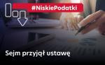 Napis Niskie Podatki Sejm przyjął ustawę plus wykresy słupkowe, długopis i dłonie.