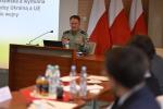 Funkcjonariusz Służby Celno-Skarbowej siedzi i omawia prezentację. W tle widoczne flagi Polski.