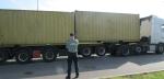 Funkcjonariusz Służby Celno-Skarbowej stoi przy samochodzie ciężarowym z dwiema przyczepami z kontenerami