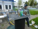 Funkcjonariusz Służby Celno-Skarbowej zlewa do kratki ściekowej alkohol ze szklanych i plastikowych butelek. W tle widoczne budynki oczyszczalni.