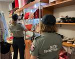 Wnętrze sklepu. Dwie funkcjonariuszki Służby Celno-Skarbowej stoją przy regałach z torebkami, odzieżą i obuwiem. 