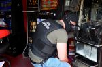 Zamaskowany funkcjonariusz Służby Celno-Skarbowej przed otwartym automatem do gier.