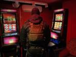 Ciemne pomieszczenie. Ubrany w kamizelkę służbową funkcjonariusz Służby Celno-Skarbowej stoi przed dwoma automatami hazardowymi 