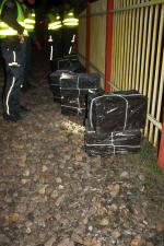 Noc. Przy płocie leży kilka owiniętych czarną folia pakunków. Obok stoi czterech funkcjonariuszy Służby Celno-Skarbowej w odblaskowych kamizelkach