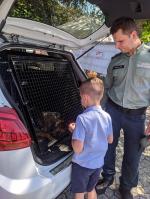 Funkcjonariusz SCS pokazuje chłopcu psa, który znajduje się w bagażniku auta.
