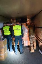 Wnętrze naczepy TIRa. Funkcjonariusze SCS i CBŚP wyjmują z kartonowego pudła paczki z papierosami