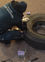 funkcjonariusz Służby Celno-Skarbowej wyjmuje z opony owinięte czarną taśmą pakiety papierosów