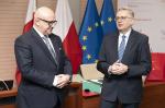 Jarosław Edeński (po lewej) i Tadeusz Gawda (po prawej) stoją w sali konferencyjnej podczas uroczystego spotkania; w tle flagi Polski i Unii Europejskiej oraz ścianka Krajowej Administracji Skarbowej.