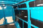 Ściana boczna przestrzeni ładunkowej niebieskiego samochodu typu bus. W przestrzeniach ukryte pakiety z papierosami owinięte czarną folia.  