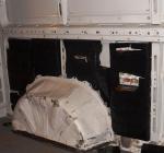 Pakiety z papierosami owinięte czarną folią ukryte w ścianach bocznych białego busa. Widok na ścianę boczną z kołem.