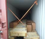 Widok na wnętrze kontenera. W środku leżące długie drewniane skrzynie a na nich ustawione kartonowe pudełka. 